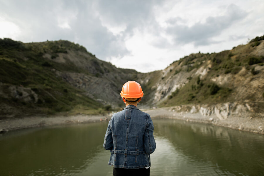 Engineer in hard hat looking at a lake in a quarry, shot from behind.