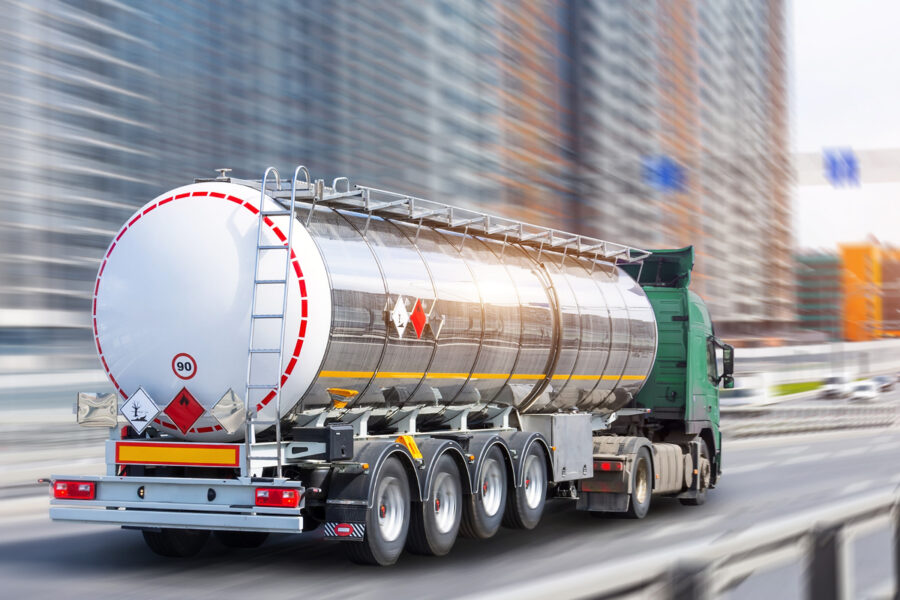 Tanker truck with hazardous goods labelling driving on a city motorway with skyscrapers in the background.